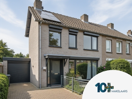 Een rijtjeswoning met bakstenen gevel en zadeldak, voorzien van zonnepanelen en donkergrijze kozijnen. Voor de woning is een voortuin met groen struikgewas en een betegelde oprit naast een garage. De lucht is helder met enkele wolken.